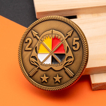 Antique bronze challenge coin featuring a shark jaw with a yellow, red, black, and white medicine wheel, crossed arrows, the numbers 2 and 5, and two stars.