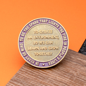 Gold challenge coin featuring a purple outer ring and raised text about creating an environment to learn and grow together.