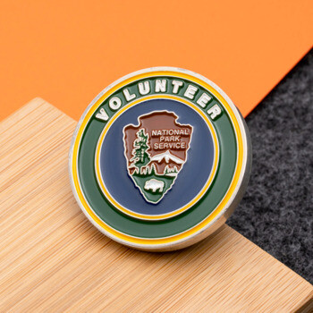 Enamel National Park Service Volunteer challenge coin featuring the arrowhead logo with green and yellow concentric circles.