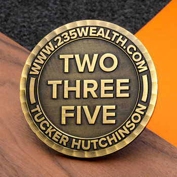 Antiqued bronze challenge coin featuring Two Three Five and Tucker Hutchinson text with a raised border, displayed on a wooden surface.