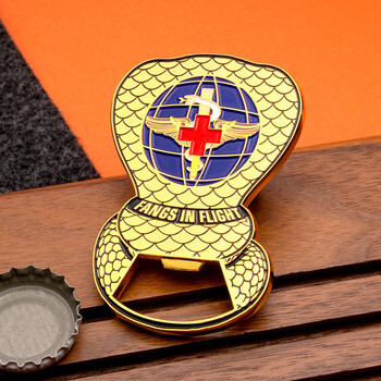 Cobra-shaped bottle opener challenge coin with Fangs In Flight text and medical insignia next to a bottle cap
