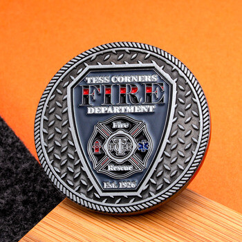 Tess Corners Fire Department challenge coin featuring a silver diamond plate texture and shield emblem with Maltese cross.