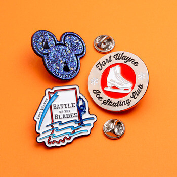 Custom enamel lapel pins for Fort Wayne Ice Skating Club, Battle of the Blades, and a glitter mouse ears design on an orange background.